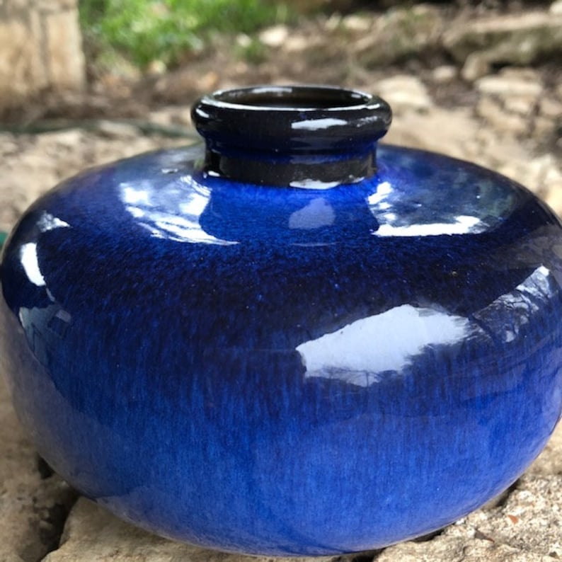 May include: A round, blue ceramic vase with a dark blue glaze. The vase has a wide mouth and a smooth, glossy finish.
