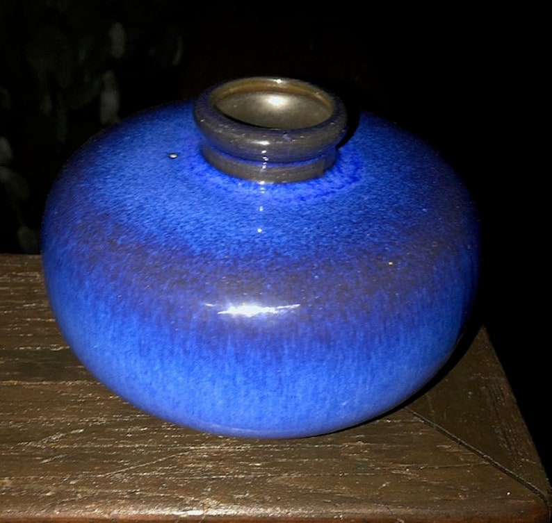 May include: A small, round, blue ceramic vase with a dark blue glaze. The vase has a wide mouth and a narrow neck.