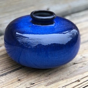 May include: A small, round, blue ceramic vase with a glossy finish. The vase has a dark blue rim.