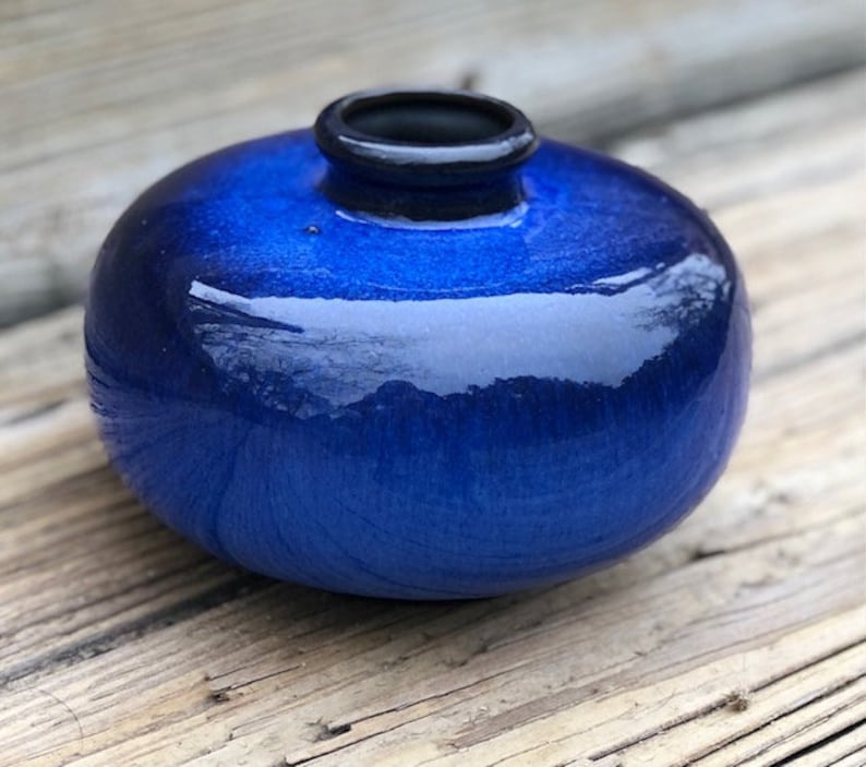 May include: A small, round, blue ceramic vase with a glossy finish. The vase has a dark blue rim.