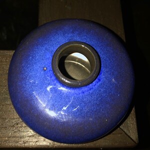 May include: A small, round, blue ceramic inkwell with a circular opening in the center.