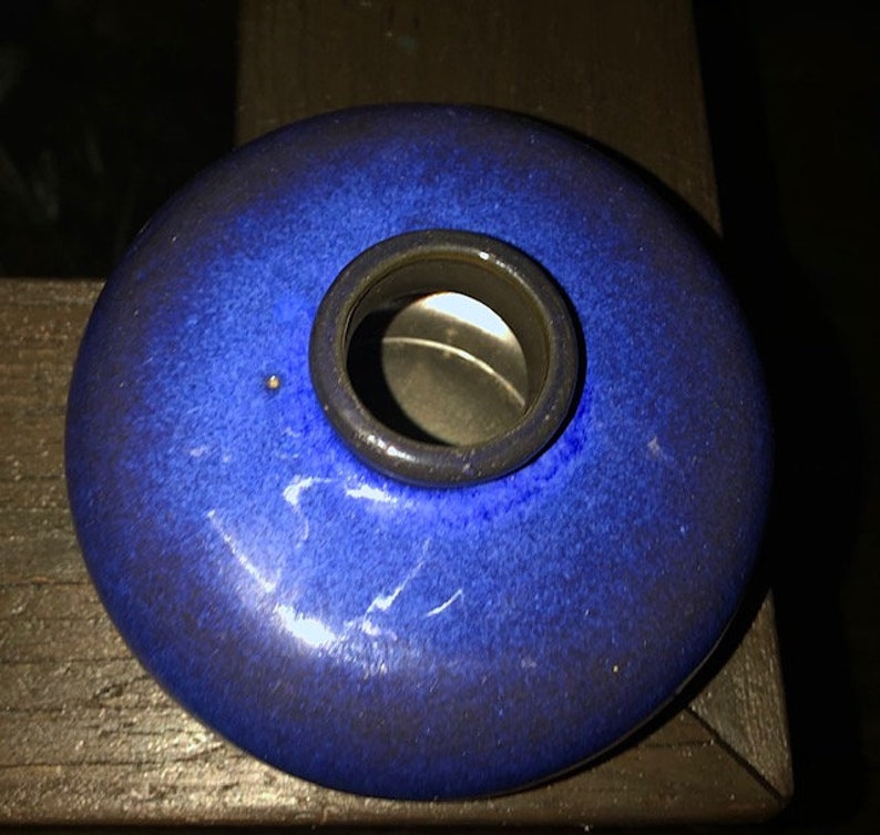 May include: A small, round, blue ceramic inkwell with a circular opening in the center.