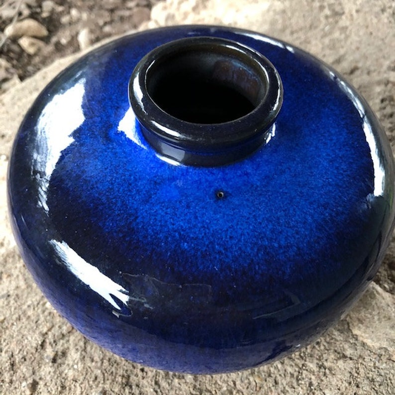 May include: A deep blue ceramic vase with a rounded shape and a dark blue rim. The vase has a glossy finish and a slight ombre effect.