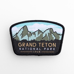 May include: A black patch with a mountain range design and the words "GRAND TETON NATIONAL PARK 1929". The patch shows a blue sky and green and grey mountains.