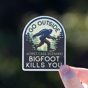 May include: A sticker with a green, blue, and yellow color scheme. It features a cartoon Bigfoot walking through a forest with the text "Go Outside Worst Case Scenario Bigfoot Kills You".