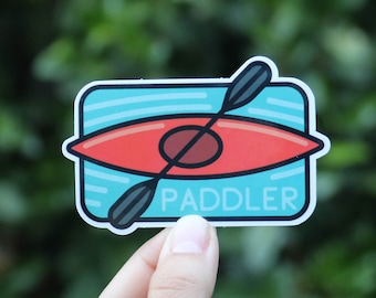 May include: A blue and red sticker with a cartoon illustration of a kayak and paddle. The sticker says "PADDLER" in white text.