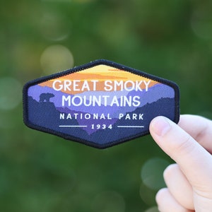 Puede incluir: Un parche negro y morado con una escena de puesta de sol y una silueta de oso. El texto dice "Great Smoky Mountains National Park 1934."