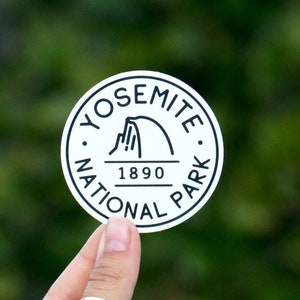 May include: A white round sticker with black text and a graphic of Half Dome. The text reads "Yosemite National Park 1890".