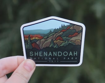 Pode incluir: Um adesivo branco com uma ilustração colorida de uma cordilheira e o texto "Shenandoah National Park 1935".