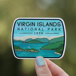 May include: A white sticker with a blue and green illustration of a landscape with islands and water. The text "VIRGIN ISLANDS NATIONAL PARK 1956" is printed on the sticker.