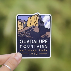 May include: A sticker featuring a stylized illustration of a mountain range with a blue sky and clouds. The text "Guadalupe Mountains National Park 1972" is printed below the image.