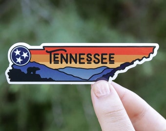May include: A sticker featuring a colorful outline of the state of Tennessee with a sunset gradient, mountains, a bear, and the text "TENNESSEE".