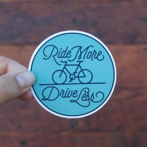 May include: A blue and white round sticker with the text "Ride More Drive Less" and a bicycle illustration.