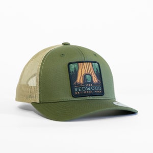 May include: A green and tan trucker hat with a patch featuring a large redwood tree and the text "1968 Redwood National Park".