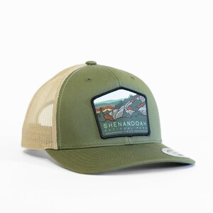 May include: A green and tan trucker hat with a patch featuring a landscape scene and the text "Shenandoah National Park 1935".