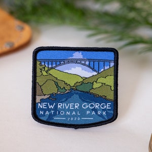 May include: A blue, green, and white embroidered patch with a bridge over a river and the text "New River Gorge National Park 2020".