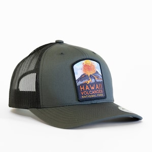 May include: A green and black trucker hat with a patch featuring a volcano erupting with the text "Hawaii Volcanoes National Park".