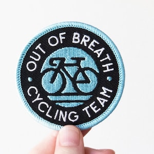 May include: A black and white embroidered patch with a blue background. The patch says "Out of Breath Cycling Team" and features a bicycle icon.