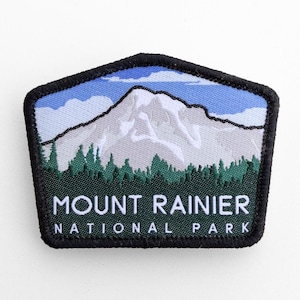 May include: Embroidered patch featuring a mountain landscape with the text "MOUNT RAINIER NATIONAL PARK." The patch has a black border, a blue sky, a white mountain, and green trees. The patch is a pentagon shape.