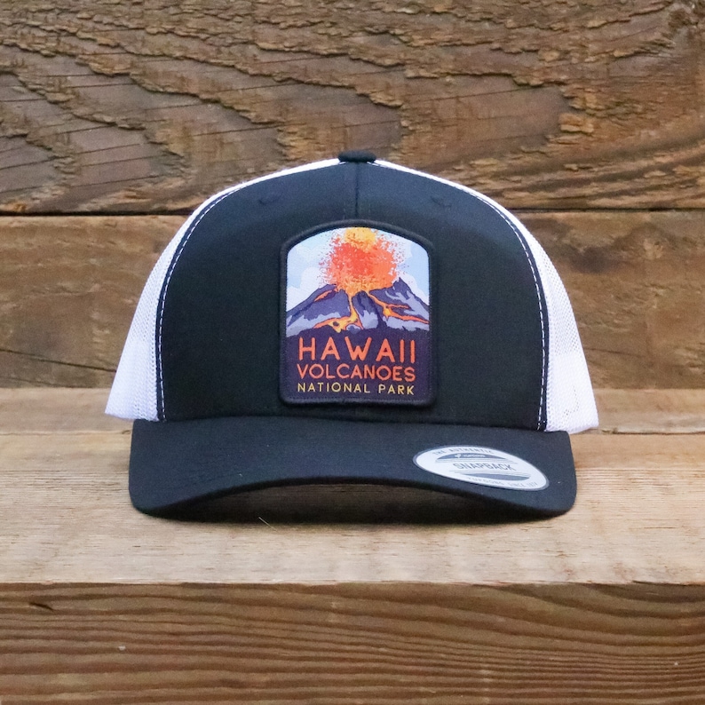 Op de afbeelding: Zwarte en witte truckercap met een patch met een uitbarstende vulkaan met de tekst "Hawaii Volcanoes National Park".