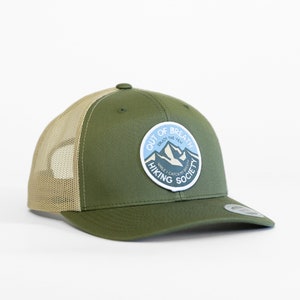 May include: A green and tan trucker hat with a patch that says "Out of Breath Enjoy the View While I Catch My Breath Hiking Society".