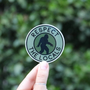 May include: A green and black round sticker with the text "Respect the Locals" and a silhouette of a Bigfoot inside a circle.