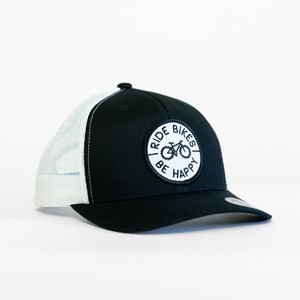 May include: Black and white trucker hat with a white patch that says "I Ride Bikes Be Happy" and a bicycle graphic.