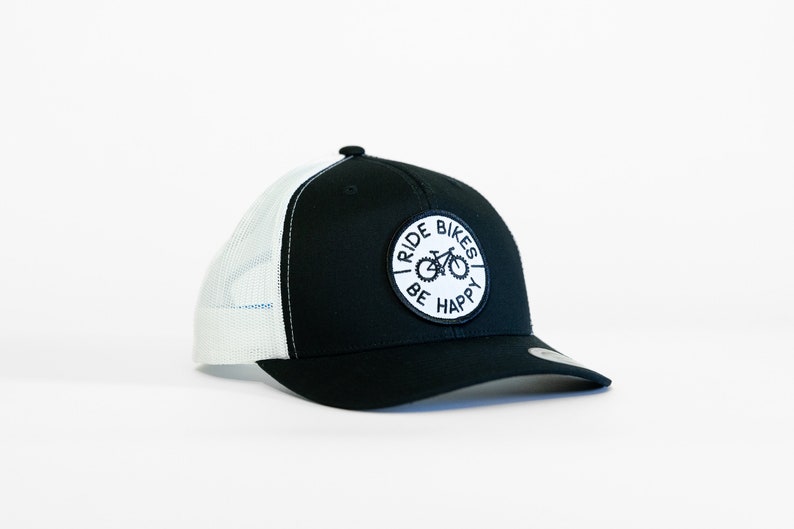 May include: Black and white trucker hat with a white patch that says "I Ride Bikes Be Happy" and a bicycle graphic.