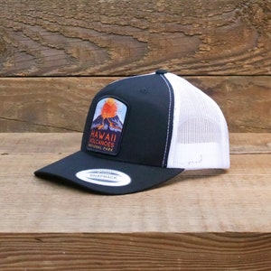 Op de afbeelding: Zwarte en witte truckercap met een patch met een vulkaan en de tekst "Hawaii Volcanoes National Park".