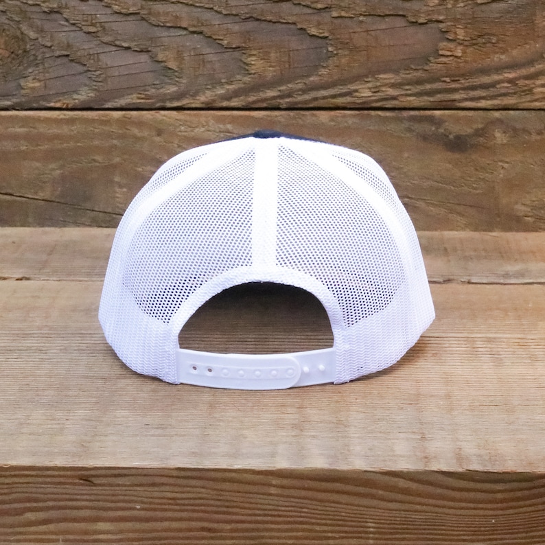 Op de afbeelding: Een witte en zwarte mesh trucker-pet met een witte verstelbare band aan de achterkant.
