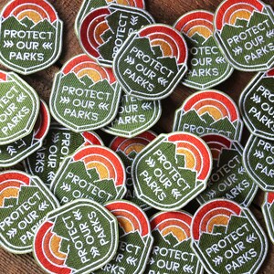Two dozen Protect Our Parks patches lie scattered across a wooden table in an overlapping pile.