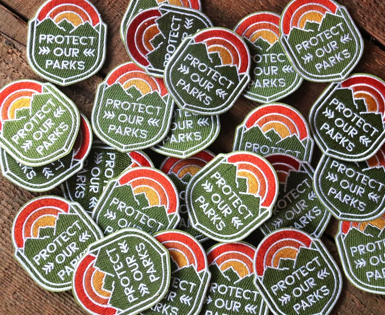 Two dozen Protect Our Parks patches lie scattered across a wooden table in an overlapping pile.