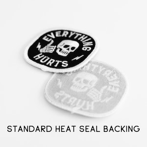 May include: Two circular embroidered patches with a black background and white border. The design features a white skull, a hand giving a thumbs up, and the text EVERYTHING HURTS. One patch shows the front, while the other shows the heat seal backing.