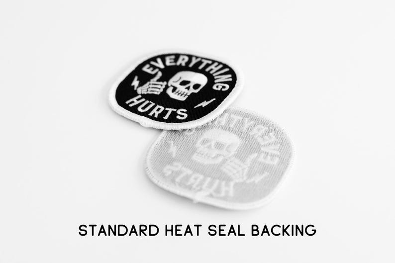 May include: Two circular embroidered patches with a black background and white border. The design features a white skull, a hand giving a thumbs up, and the text EVERYTHING HURTS. One patch shows the front, while the other shows the heat seal backing.
