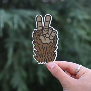 May include: A brown furry hand making the peace sign. The hand is outlined in black and has a white background.