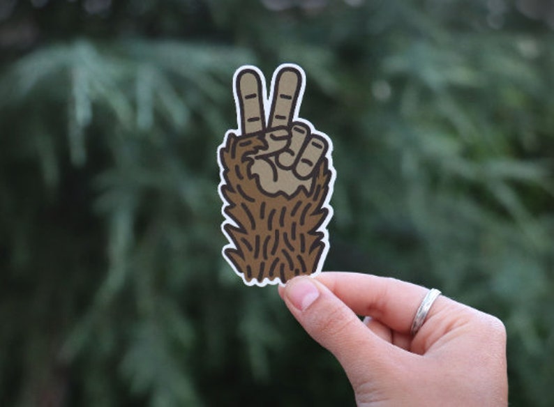 May include: A brown furry hand making the peace sign. The hand is outlined in black and has a white background.