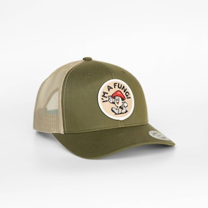May include: An olive green trucker hat with a beige mesh back and a circular patch on the front. The patch features a cartoon mushroom character with a red cap, white gloves, and shoes, accompanied by the text I'M A FUNGI in black lettering.