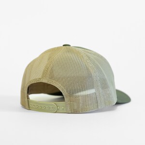 May include: A green and beige mesh trucker hat with a plastic adjustable strap in the back.