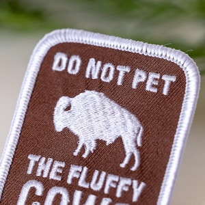 Peut inclure: Patch en tissu marron avec du texte brod&eacute; blanc qui dit "Ne pas caresser les vaches moelleuses". Le patch pr&eacute;sente une image brod&eacute;e blanche d'un bison.