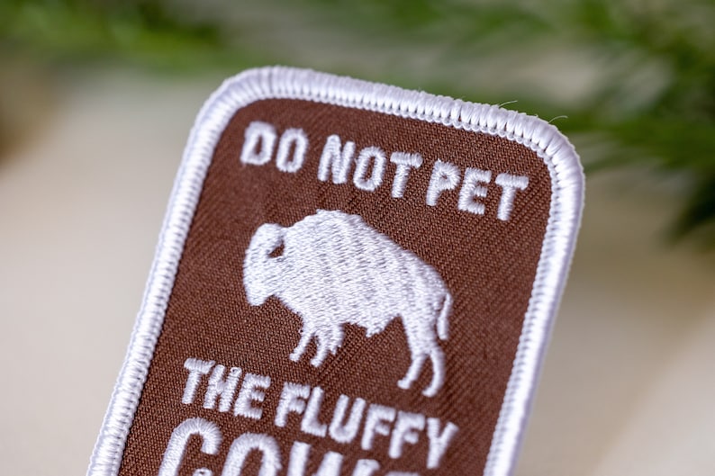 Peut inclure: Patch en tissu marron avec du texte brod&eacute; blanc qui dit "Ne pas caresser les vaches moelleuses". Le patch pr&eacute;sente une image brod&eacute;e blanche d'un bison.