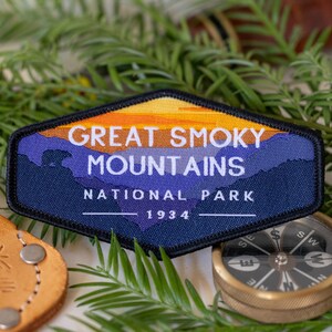 Puede incluir: Un parche bordado azul y naranja con el texto "Great Smoky Mountains National Park 1934". El parche presenta una silueta de monta&ntilde;as y una puesta de sol.