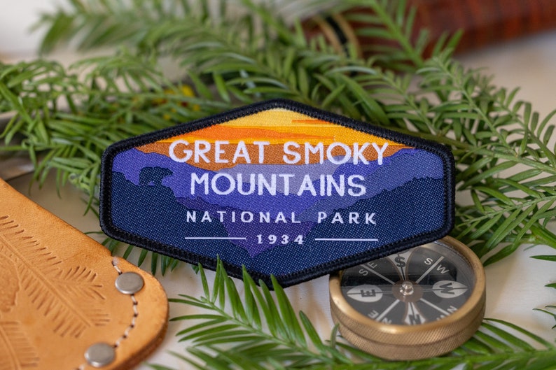 Puede incluir: Un parche bordado azul y naranja con el texto "Great Smoky Mountains National Park 1934". El parche presenta una silueta de monta&ntilde;as y una puesta de sol.