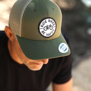 May include: A green and tan trucker hat with a black and white patch that says "Ride Bikes Be Happy" and a black and white sticker that says "The Original Snapback".