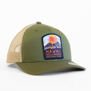 Op de afbeelding: Een groene en bruine truckercap met een patch met een uitbarstende vulkaan en de tekst "Hawaii Volcanoes National Park".