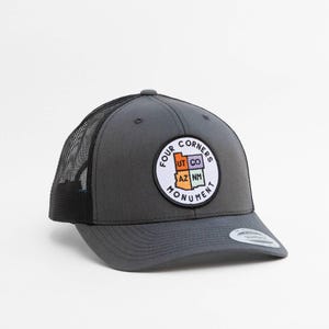 May include: A charcoal gray trucker hat with a black mesh back and a circular patch on the front. The patch features the text Four Corners Monument and a map graphic with the states of Utah, Colorado, Arizona, and New Mexico in different colors.