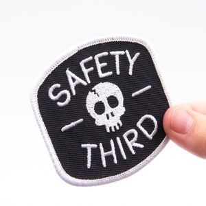 A thumb steadies the Safety Third patch at its corner, filling the frame against clean white.