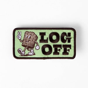 Peut inclure: Un écusson rectangulaire brodé avec un fond vert clair et une bordure marron foncé. Il représente un personnage en forme de bûche faisant un signe de paix et le texte marron foncé LOG OFF. Le personnage a des détails de bois et des gants blancs.