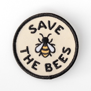 May include: A circular embroidered patch with a cream-colored background and a black stitched border. The center features a small bee with yellow and black stripes and white wings. The text "SAVE THE BEES" is stitched in black around the bee.