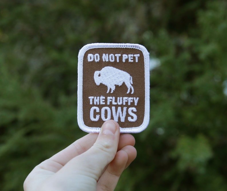 Peut inclure: Un &eacute;cusson marron avec des coutures blanches indique "Ne pas caresser les vaches moelleuses" avec une silhouette blanche de bison &agrave; l'int&eacute;rieur.