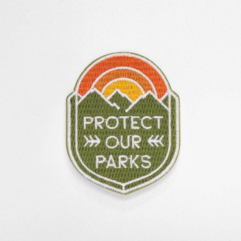 Flat on white, the green Protect Our Parks patch shows its stitched mountains under an orange and yellow sun.